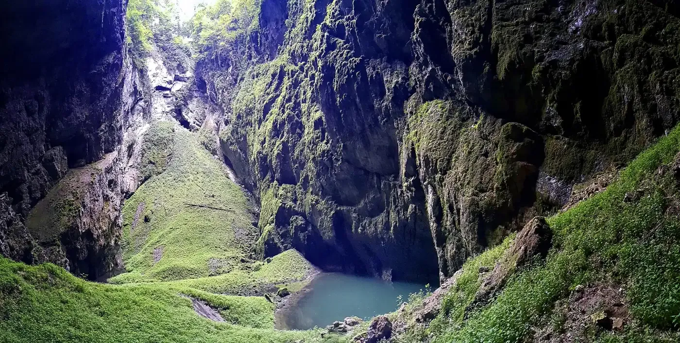Blick vom Grund der Schlucht Macocha auf steile Felswände und den grünen Teich